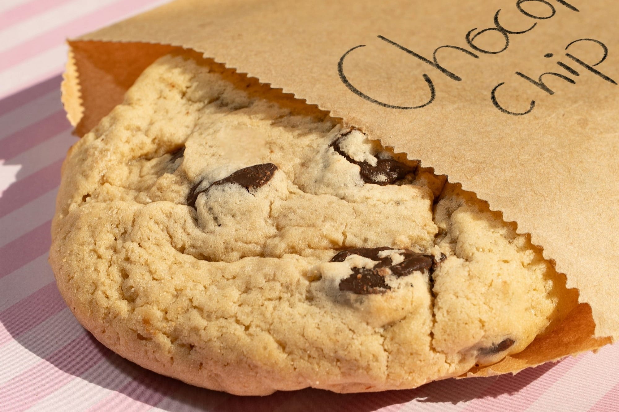 A chocolate chip cookie in a brown paper bag.